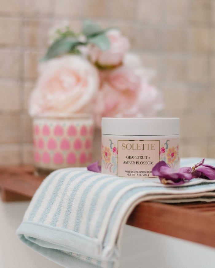 spa night at home scene with a bubble bath, flowers, a candle, and a body scrub