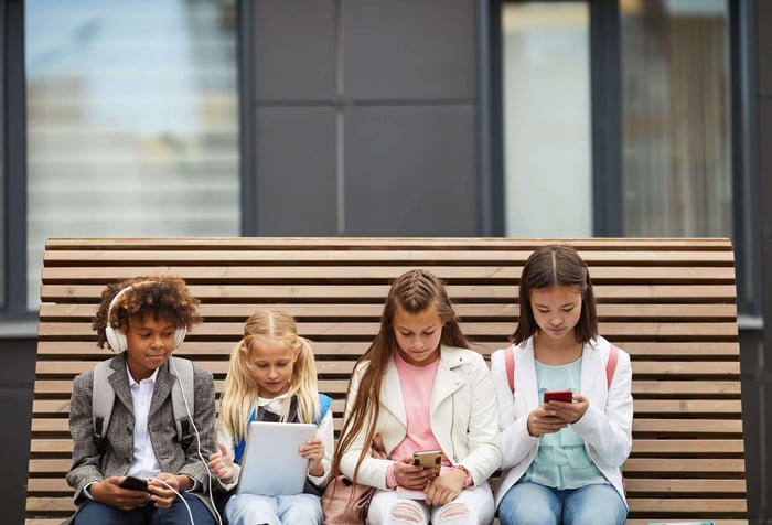 Gen Alpha kids on a bench looking at their phones. That's why murder mystery parties are better for their social life.