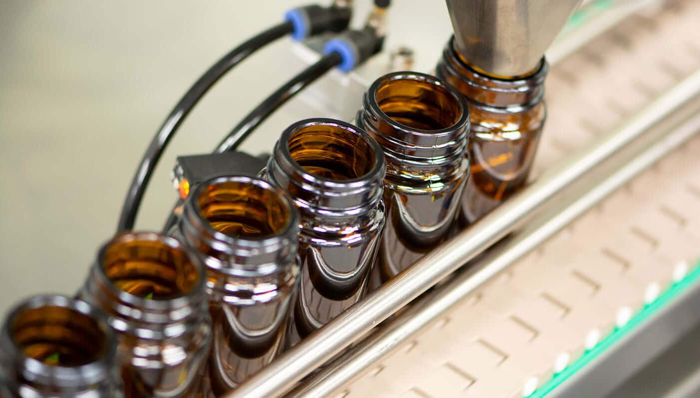 Row of amber glass bottles moving along a filling line toward a nozzle