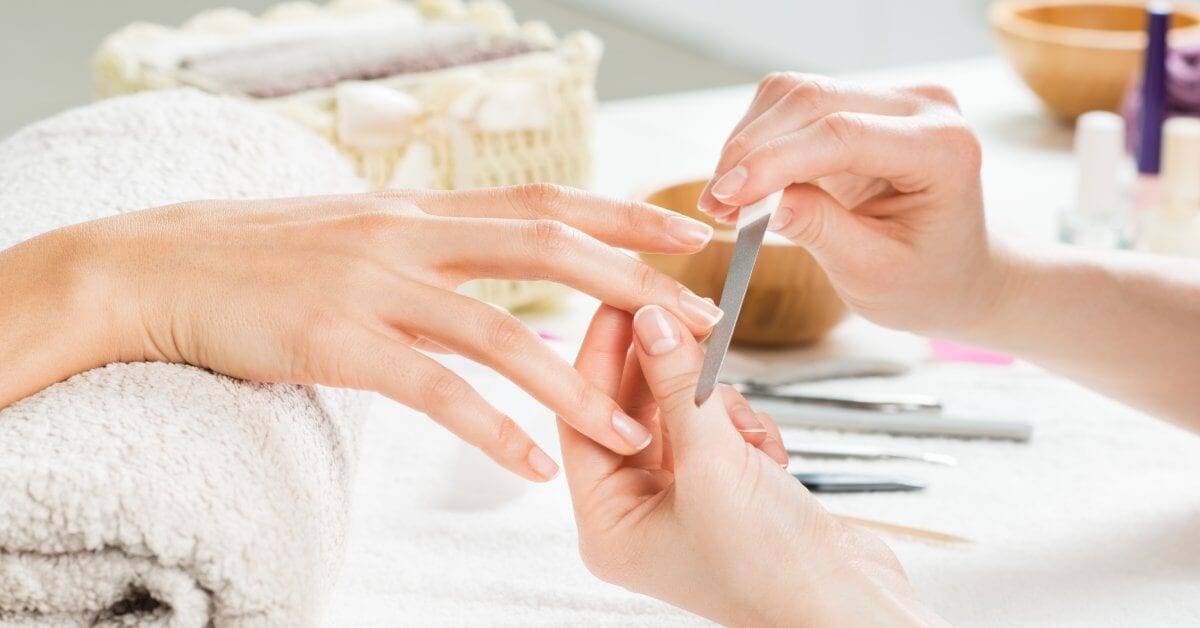 A close-up of a manicure treatment at a nail salon. The nail tech is filing the customer's natural nails.