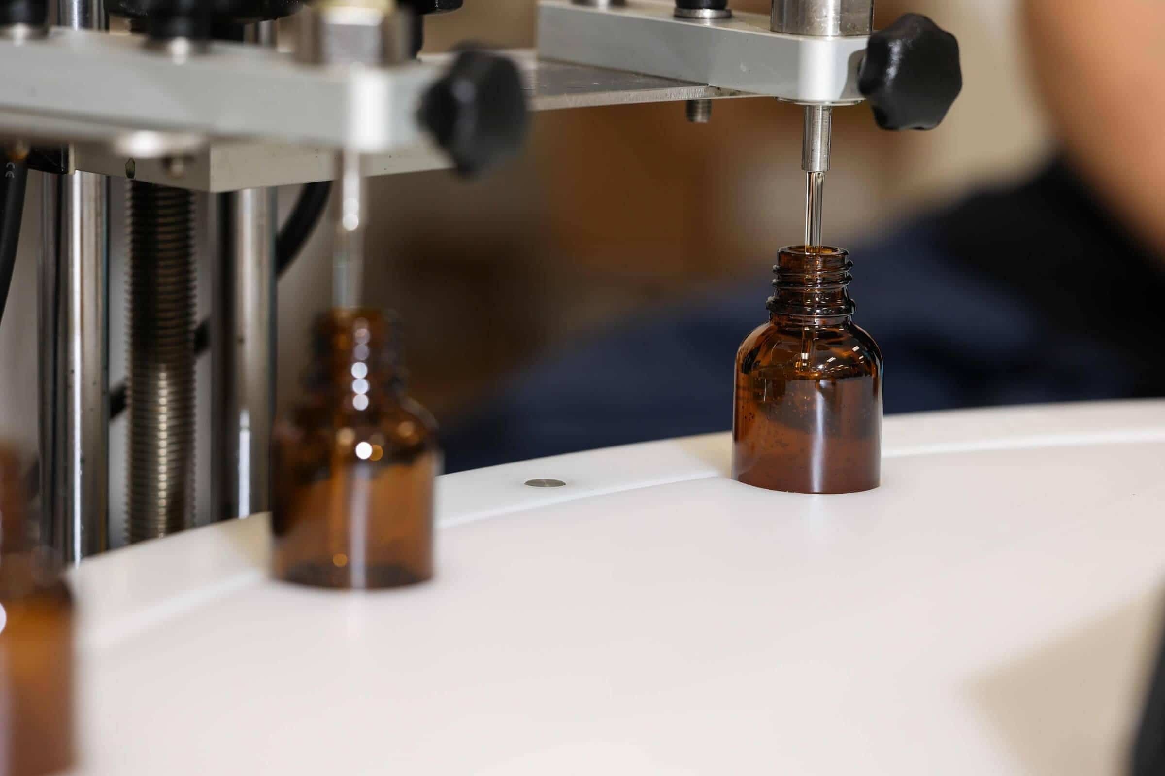 Amber glass dropper bottles being filled by a nozzle on a white bottling machine