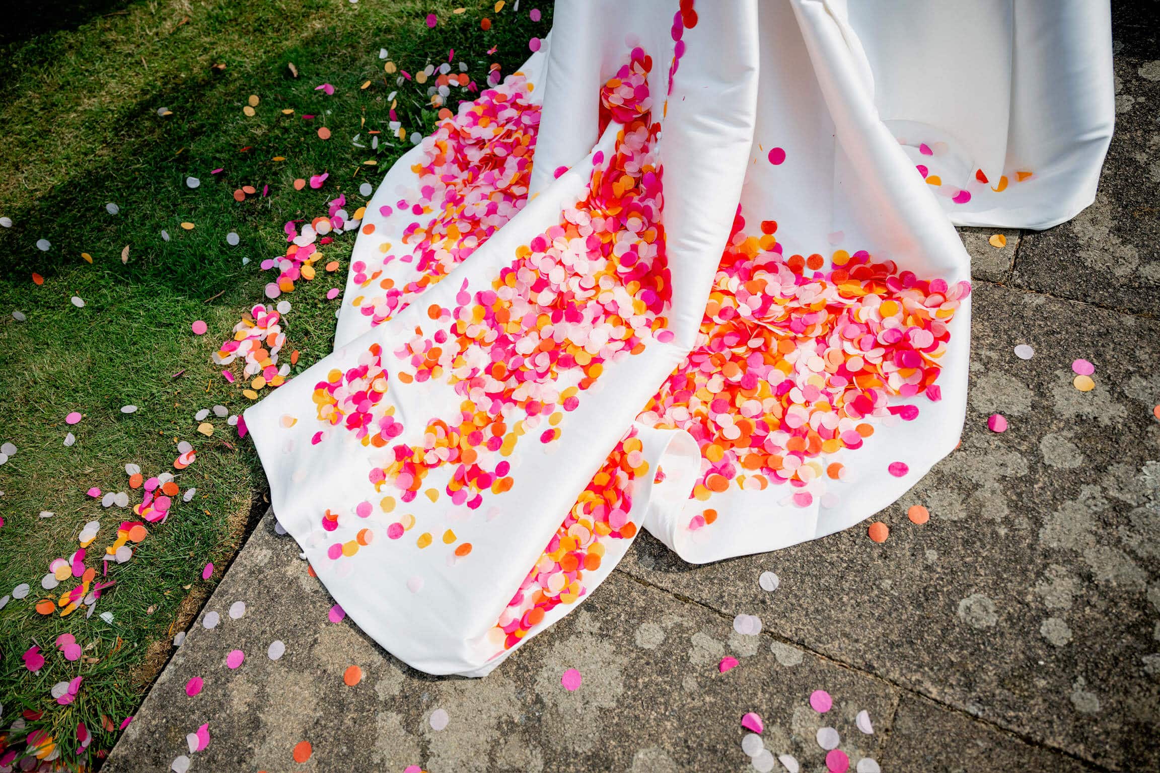 A train of a white wedding dress full of wedding confetti circles in shades of pink and orange