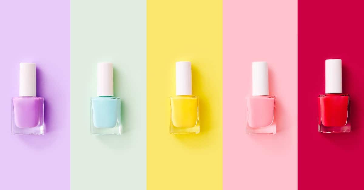 Five nail polish bottles sit against a background of a coordinating color. There are purple, blue, yellow, pink, and red.