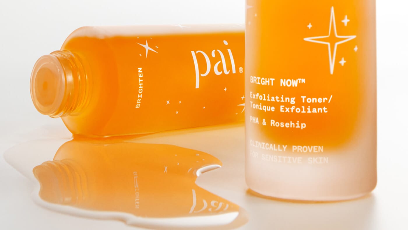 Close up image of two bottles of orange Pai Bright Now Exfoliating Toner, one on its side, left, and the base of the second, right