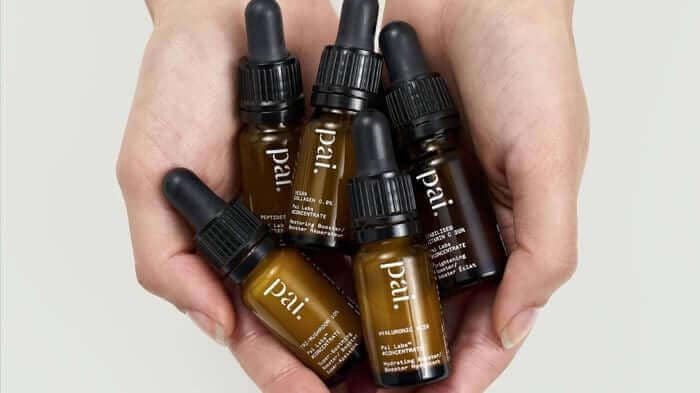 Hands holding five amber glass dropper bottles of Pai face oils and serums with black droppers, natural skincare for sensitive skin