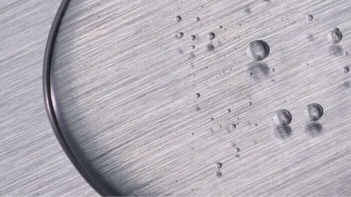 Clear water droplets beading on brushed metal surface showing hydrophobic properties