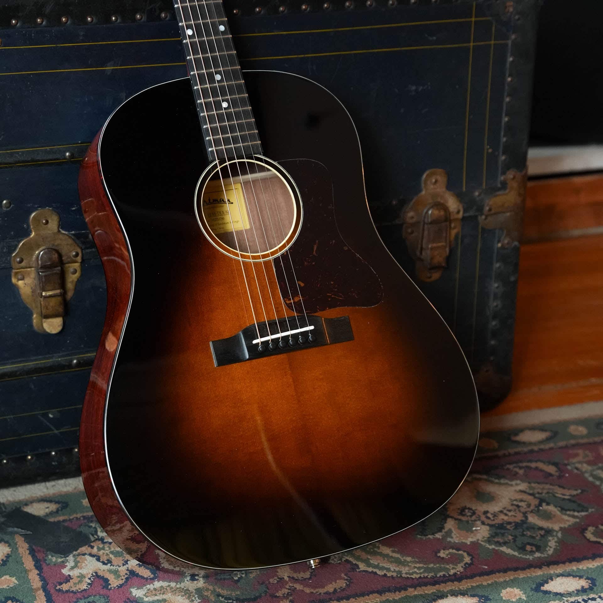 Eastman Deluxe series E1SS-DLX-SB slope shoulder dreadnought in gloss sunburst, leaning on a vintage trunk