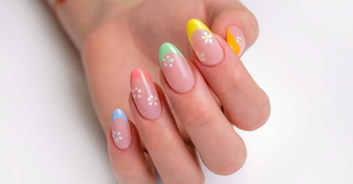 A close-up view shows a woman's hand with beautifully painted nails. The nails have colorful tips and flowers.