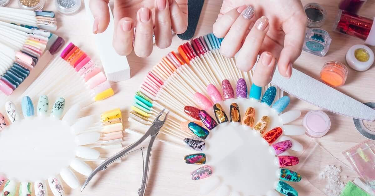 A person showing off their manicure with one decorated nail. The table is full of decorated faux nails and nail tools.