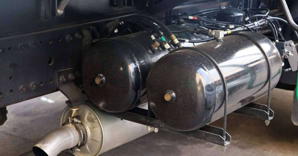 Black horizontal air receiver tanks mounted beneath a truck chassis with connected air lines and exhaust components.