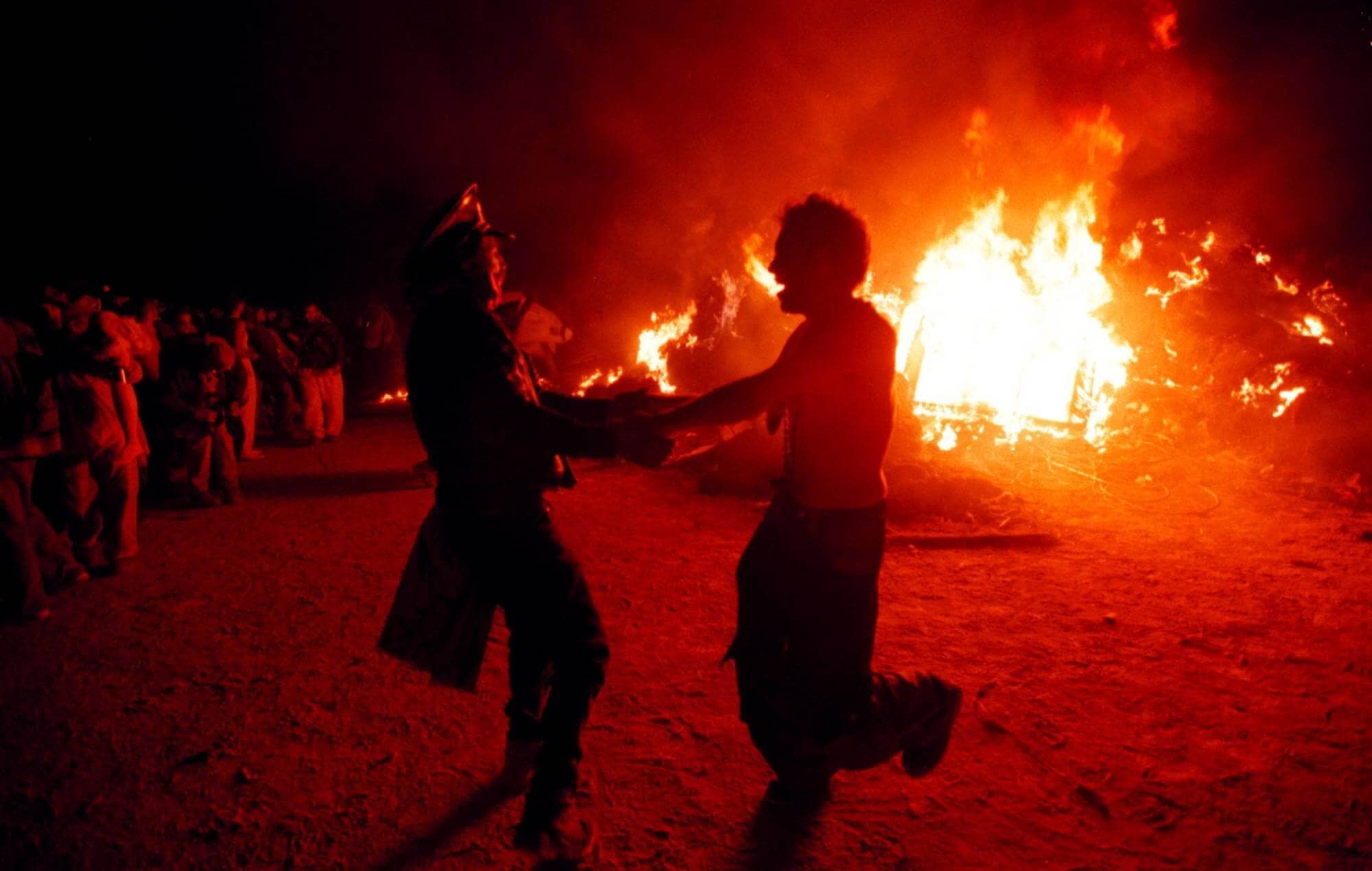 Burning Man Festival crowd and wooden effigy burning at dusk