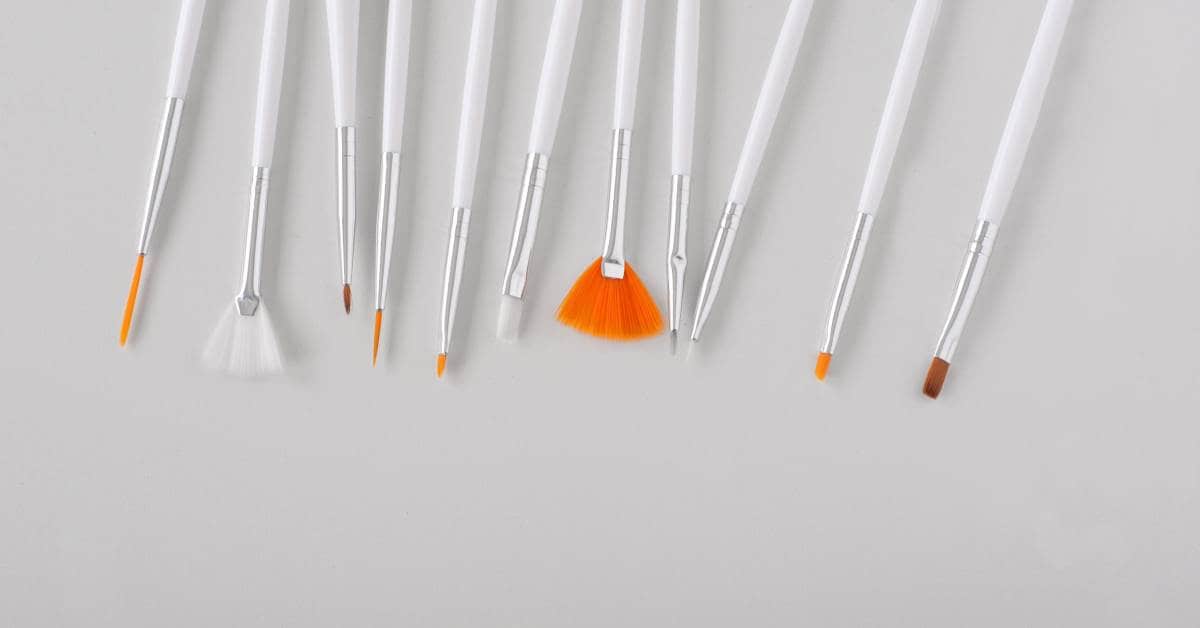 A set of 11 white nail art brushes lying beside one another, each with a different shape for varying designs.