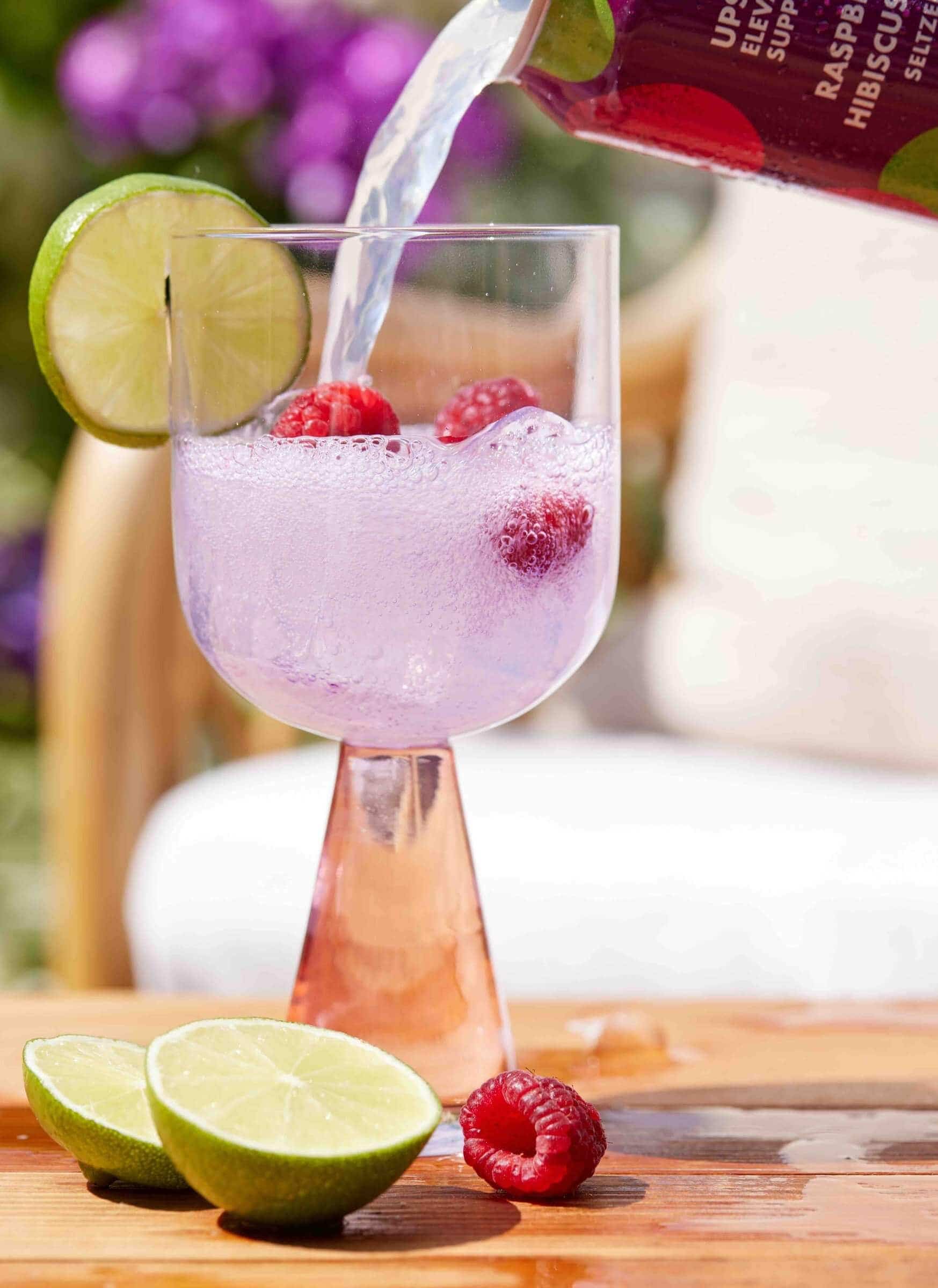 Upstate Elevator Raspberry Hibiscus seltzer being poured into a stemmed glass with lime and raspberries