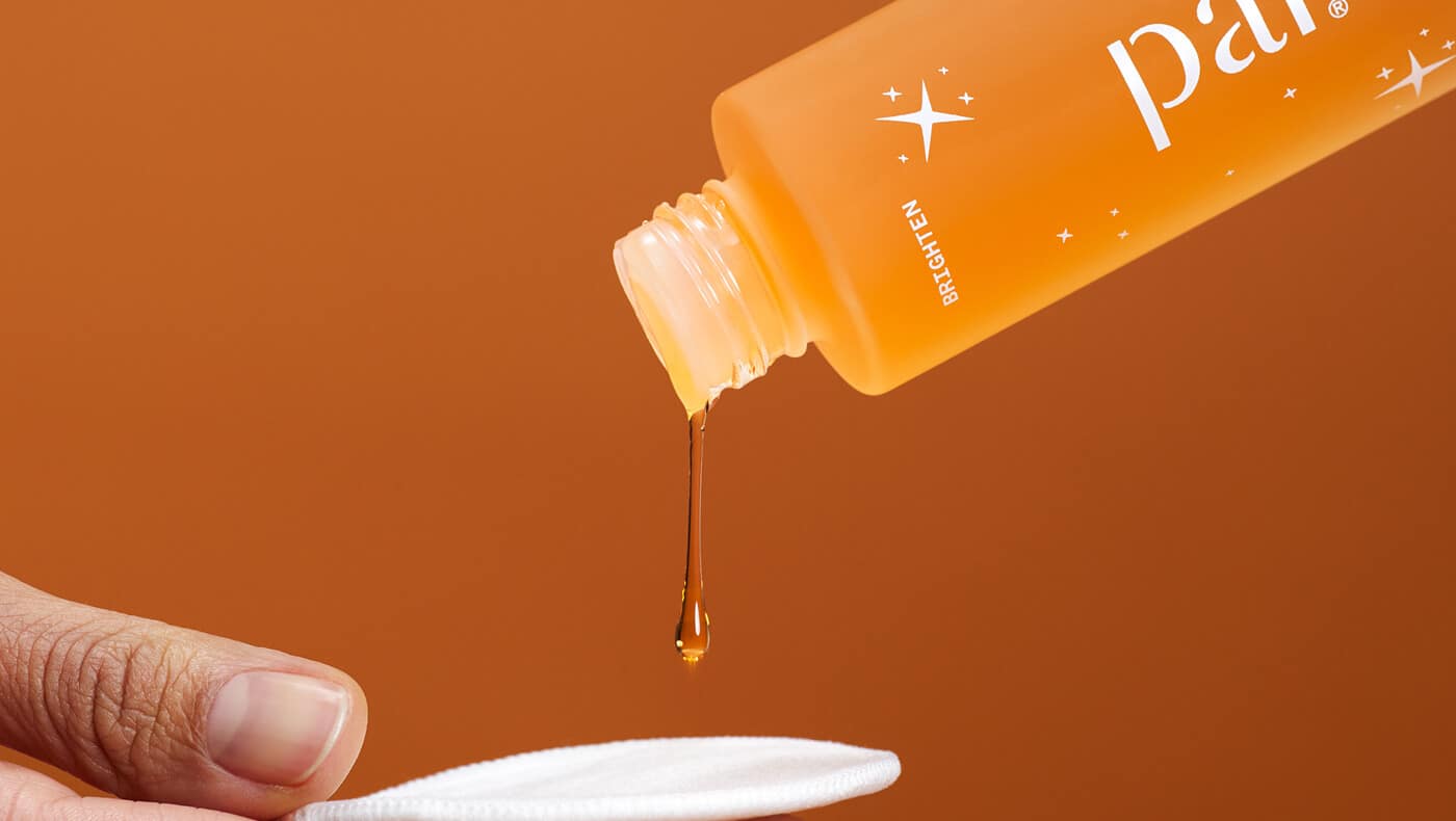 Close up of a bottle of the orange Pai Bright Now Exfoliating Toner being poured onto a reusable cotton pad