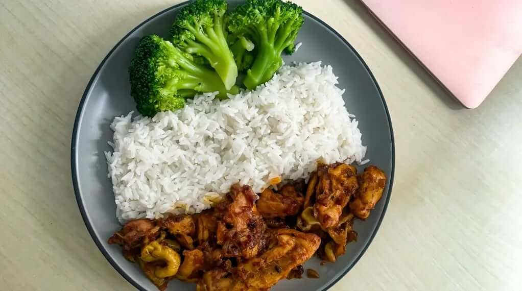 High protein chicken veggie plate with spicy stir-fried chicken, steamed white rice, and fresh broccoli florets on a grey plate.