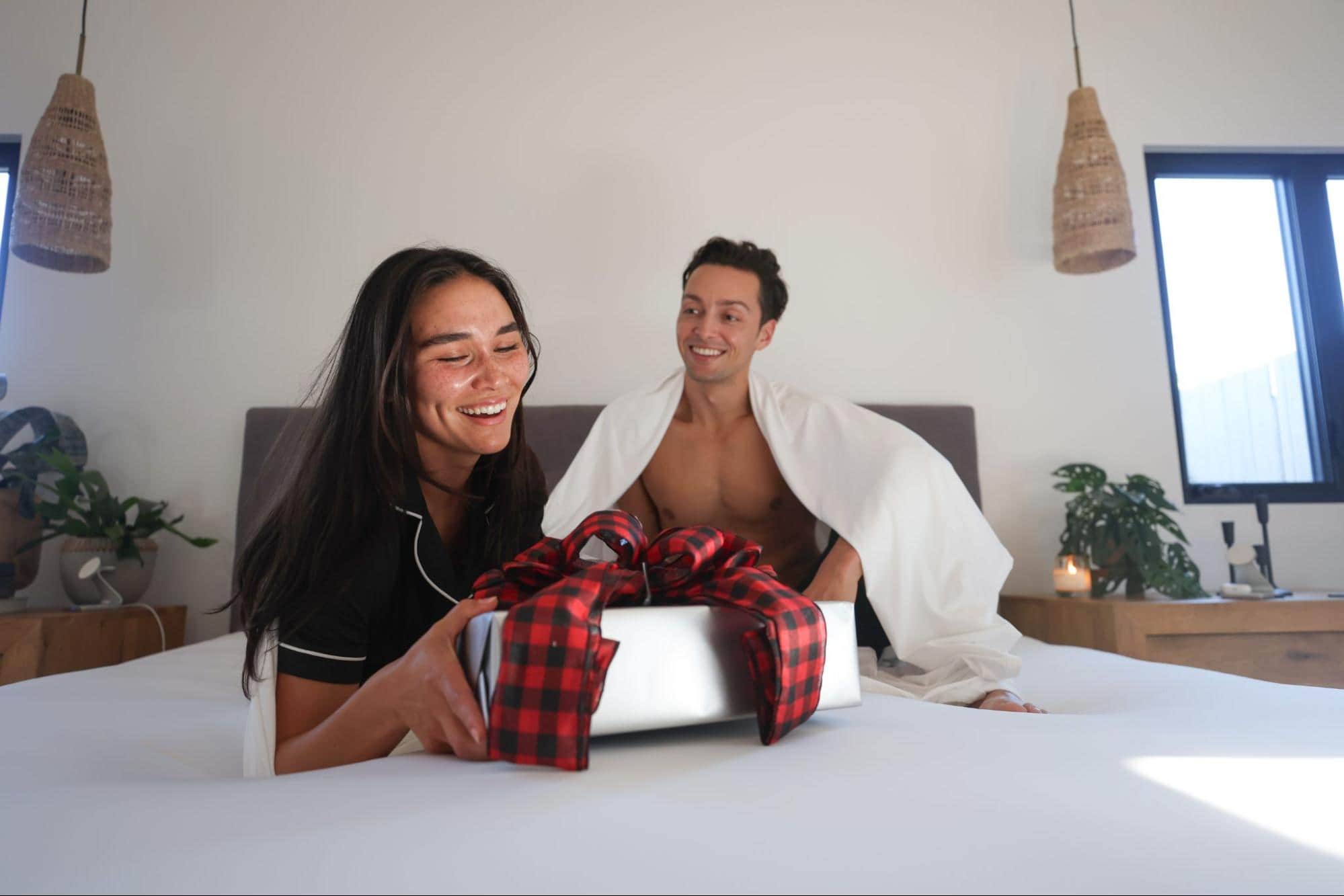 A Couple Opening Up a Holiday Present Laying on SHEEX Bedding