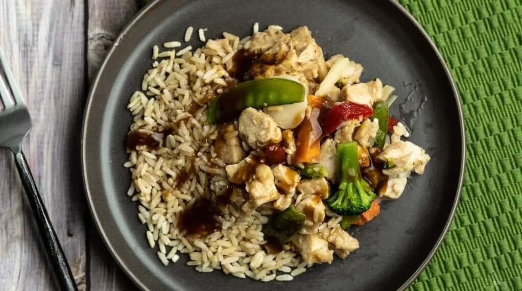 Low-calorie meal showing lean chicken stir fry with vegetables over brown rice, served on a simple plate