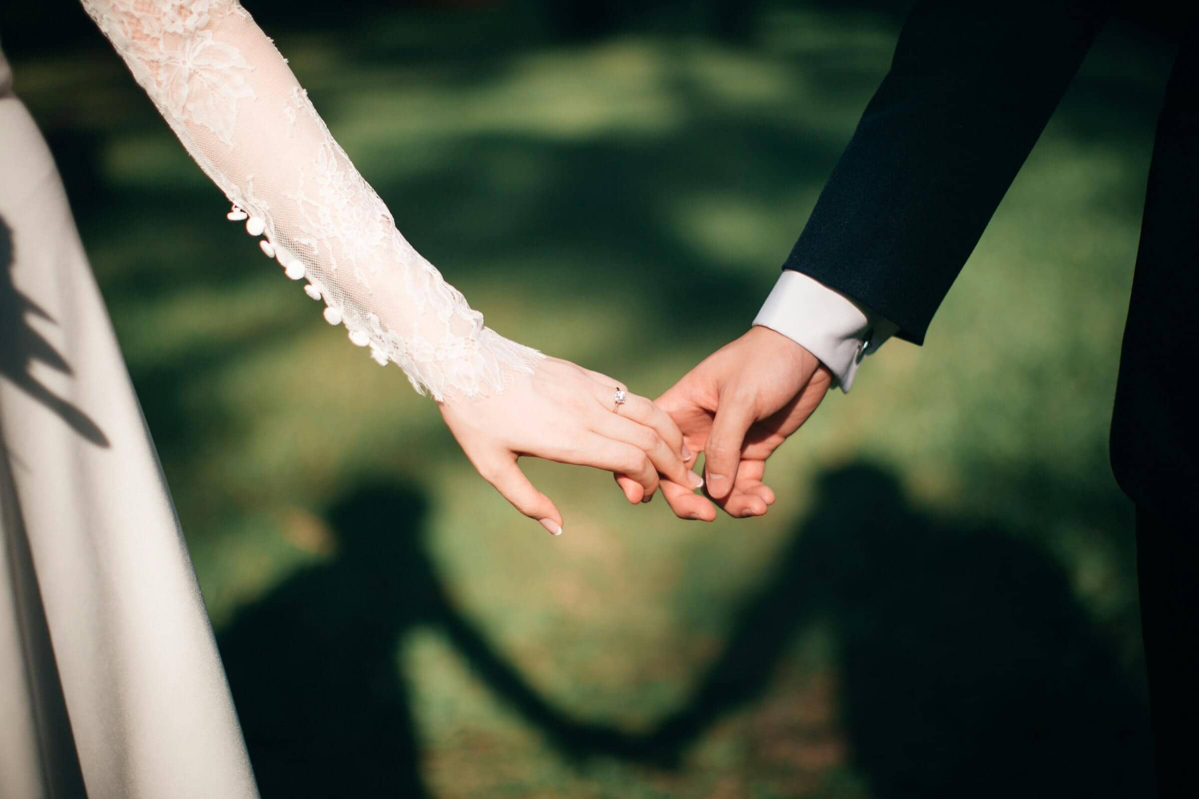 hands of bride and groom, holding hands outdoors in sunlight