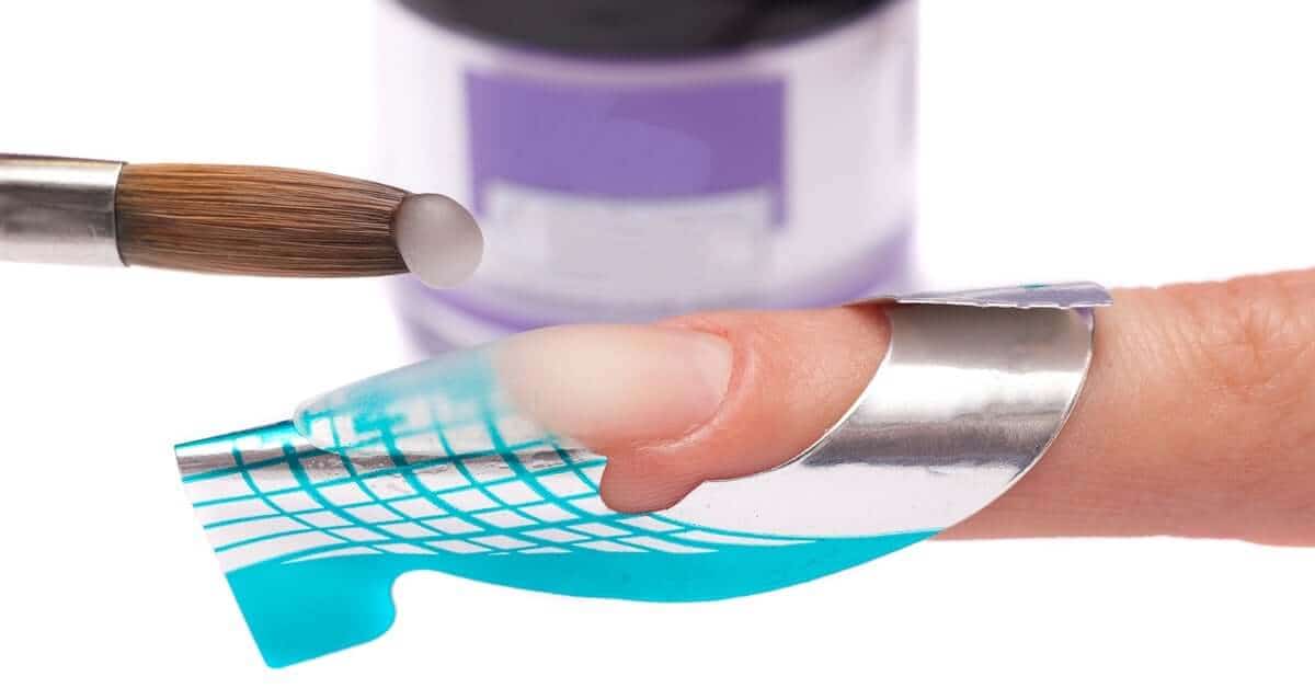 A technician applies a silver-and-blue extension form on a finger, prepping the acrylic overlay over the bare nail carefully.