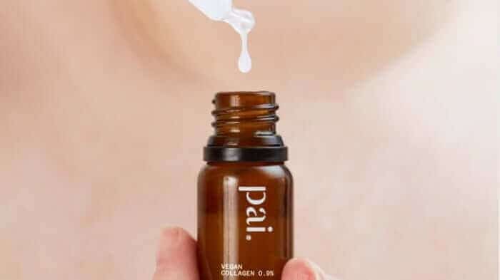 Hand holding amber glass dropper bottle of Pai Vegan Collagen serum with white dropper dispensing product
