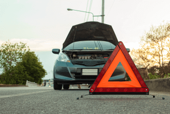 Triángulo de emergencia colocado en la carretera en frente de un coche averiado