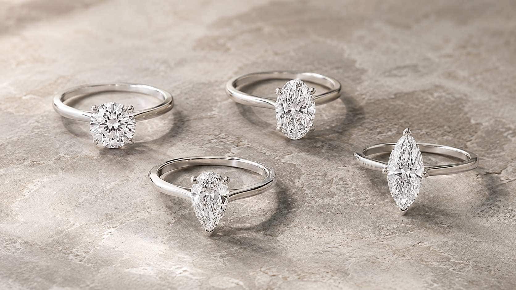 Four white-gold solitaire rings with round, oval, pear and marquise lab-grown diamond centre stones, showing differences in visible spread.