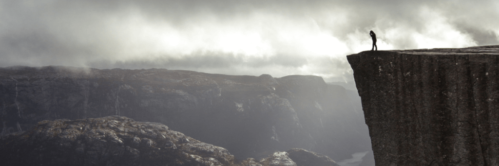 A black and white photo of a person looking hesitant or apprehensive, standing at the edge of a cliff or precipice, representing the boundary created by fear.