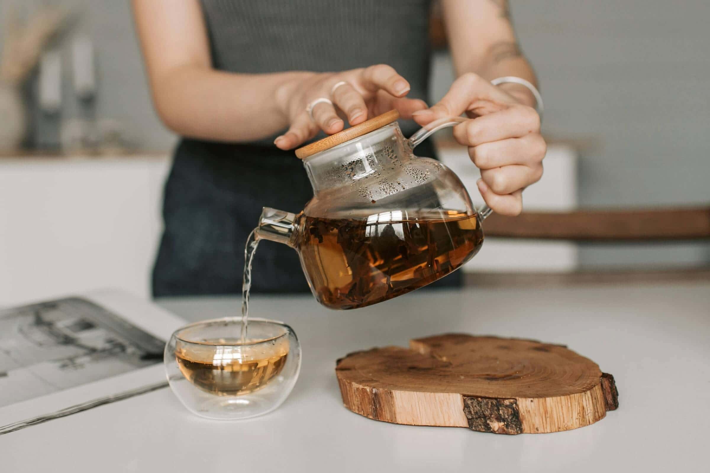Woman pouring tea from glass teapot.