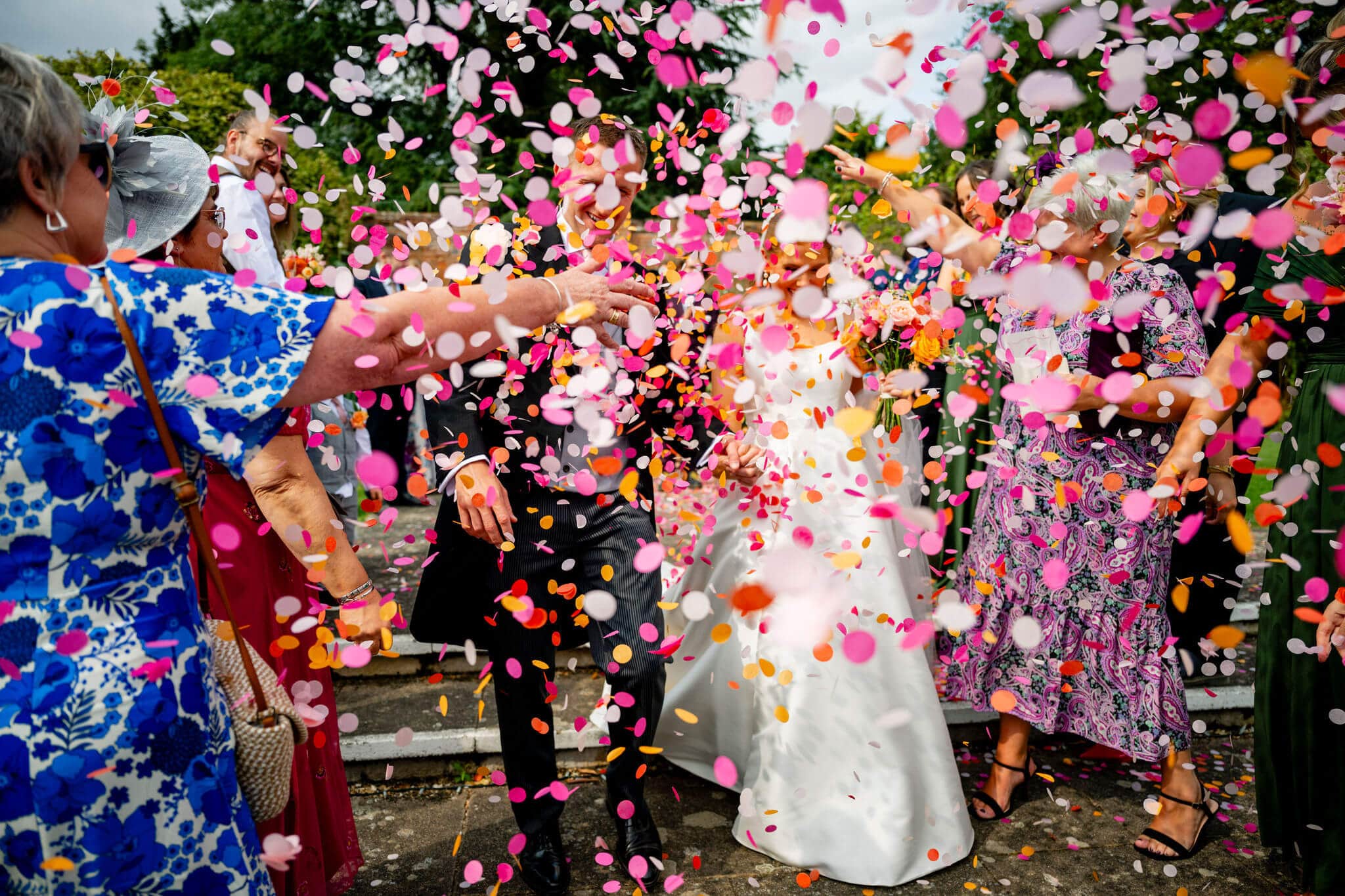 A bride ande groom are hardly visible amongst a storm of orange and pink wedding confetti