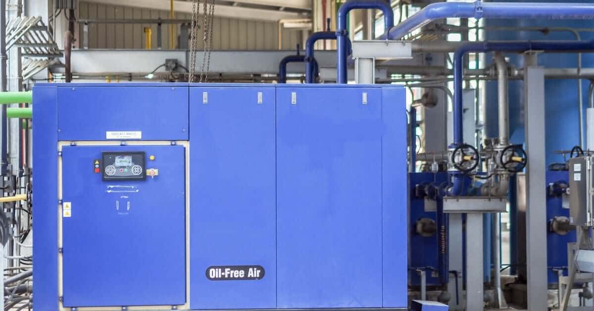 A large blue air compressor system with a control panel on the front and multiple pipes in the background.