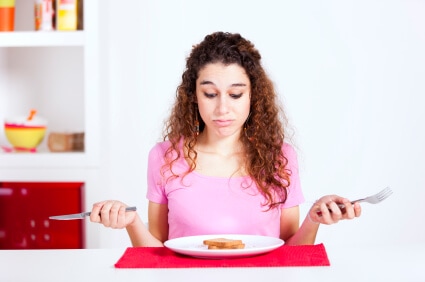 Woman with curly hair looking confused while choosing between two plates of food on kitchen counter