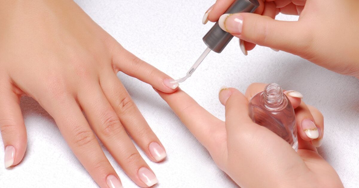 A close-up of someone getting their nails done by a professional nail tech. The nail tech is applying clear nail polish.