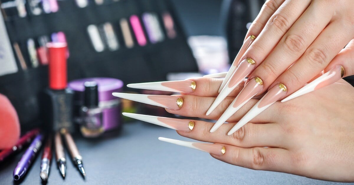 A nail client showing off their long stiletto-style nails with extended white French tips and gold cuticles.