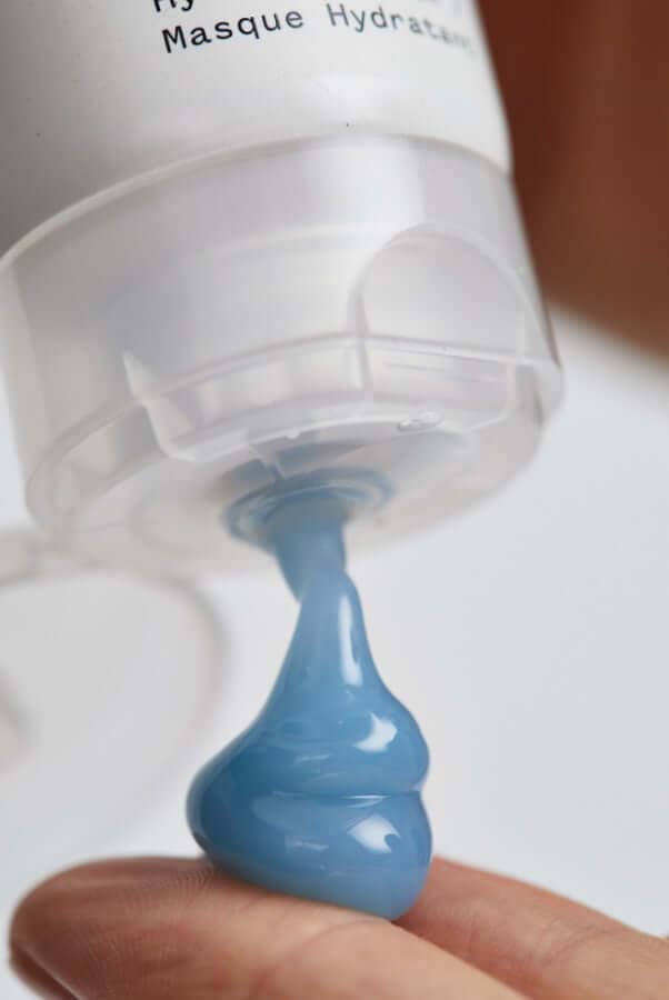 Blue hydrating face mask being dispensed from Resurrection Girl pump bottle onto fingertip
