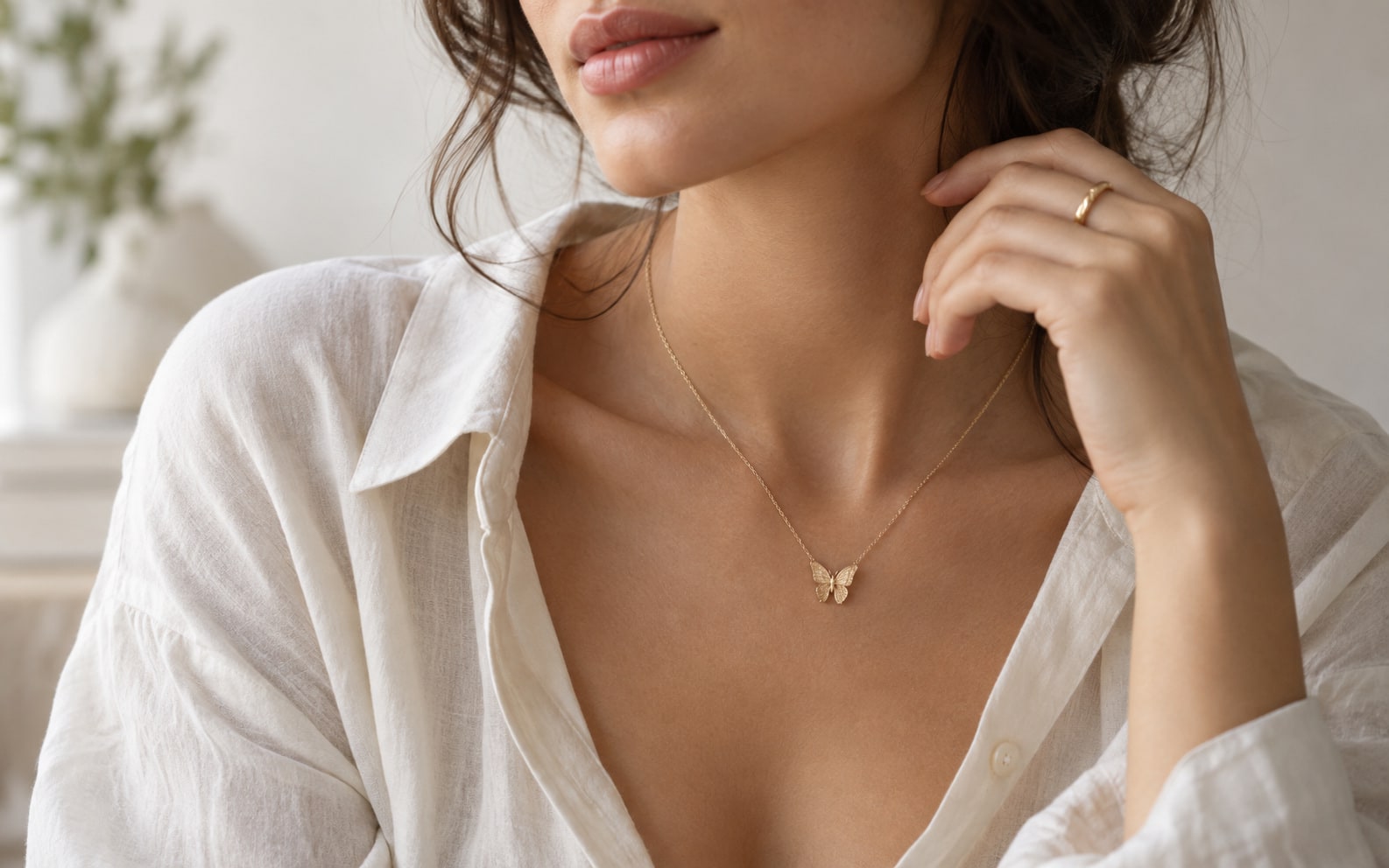 A small butterfly pendant worn with an open white shirt and a simple gold-tone ring.