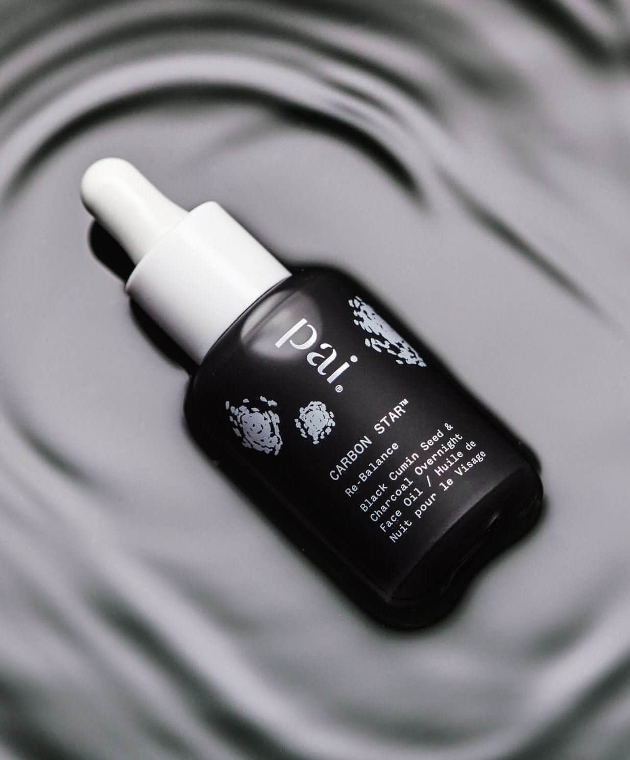 Pai Carbon Star black currant seed face oil with white dropper cap on circular mirror surface