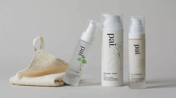 Pai Skincare cleanser and serum in white pump bottles with natural loofah sponge on neutral background