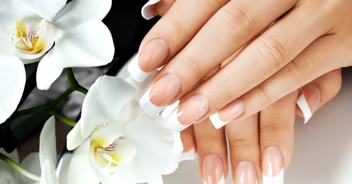 A pair of hands with white acrylic nails is next to white flowers with a yellow center and long green stems.