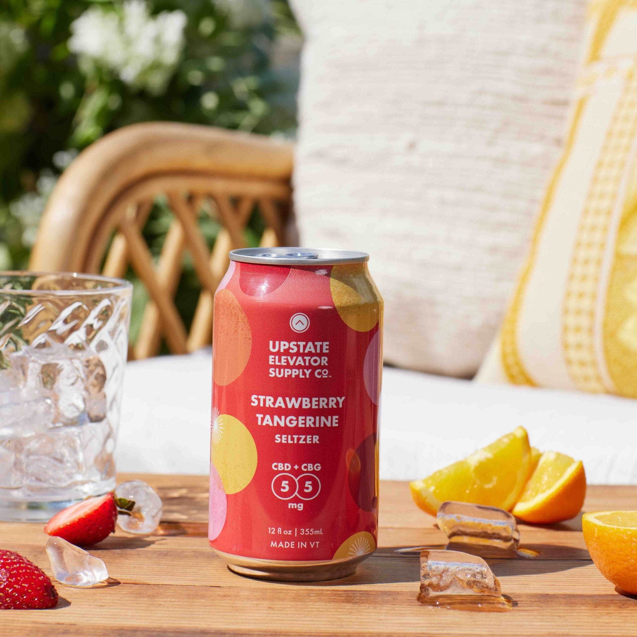 Upstate Elevator Strawberry Tangerine CBD and CBG seltzer can on a table with ice, orange wedges and strawberries