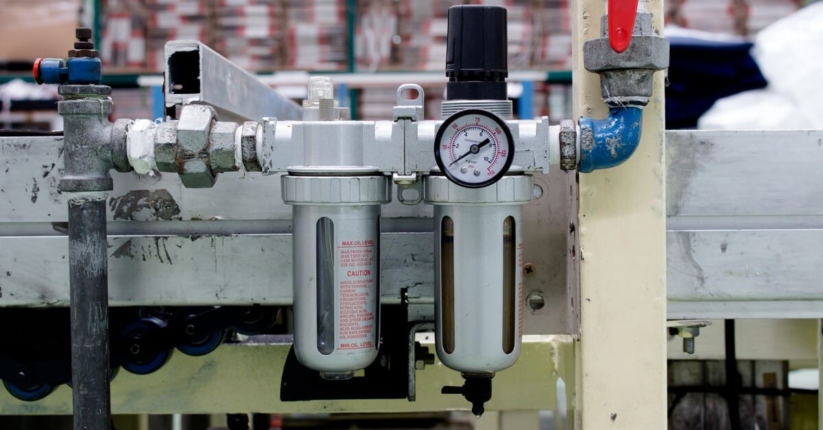 A silver and black pneumatic air filter with a numbered gauge attached to a piece of industrial equipment.
