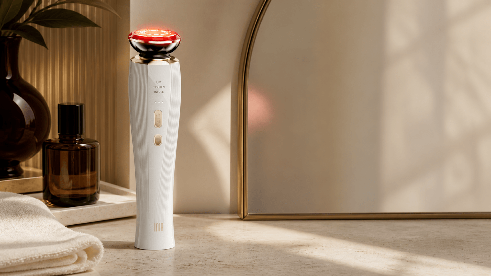 INIA FLARE Microcurrent Facial Device on a bathroom vanity beside a folded towel and mirror