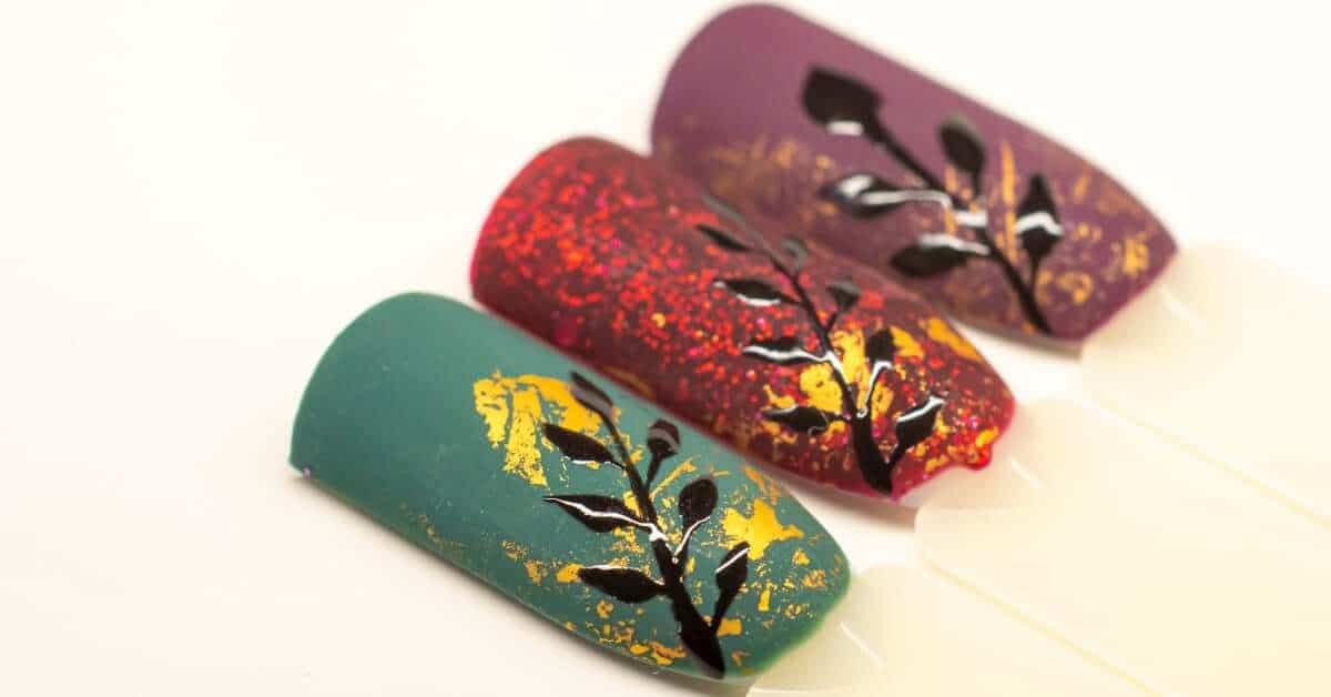 A set of three example nails in jewel tones, including green, red, and purple, with gold foil accents on each.