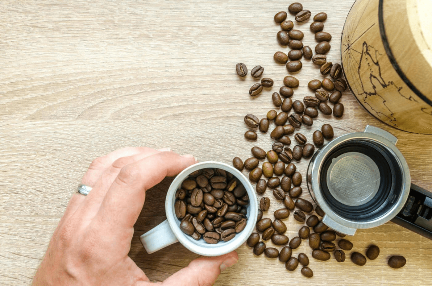 Hand holding coffee cup with beans and portafilter overhead view.