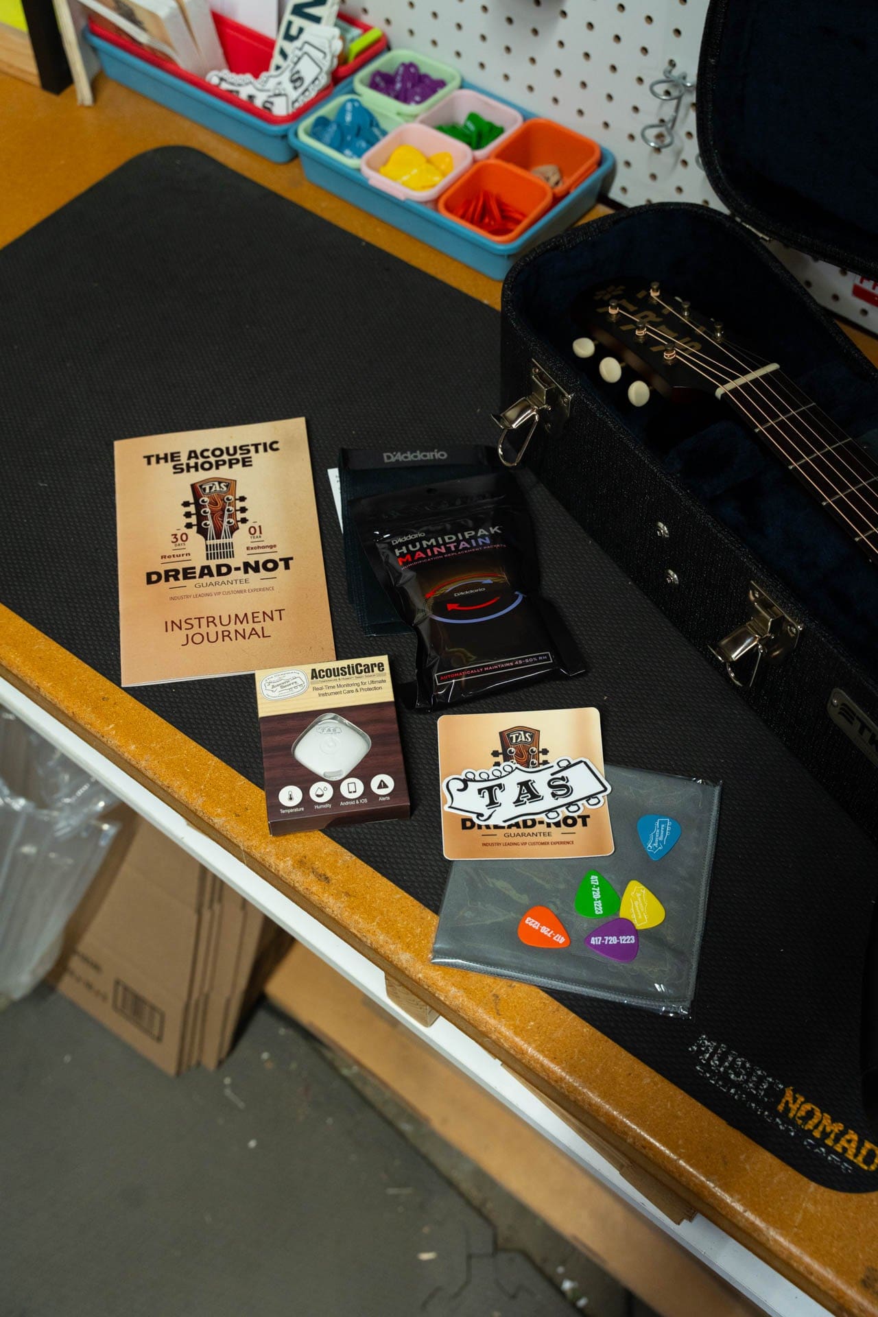Dread-Not instrument journal, humidity pack, sensor and TAS picks laid beside an open guitar case
