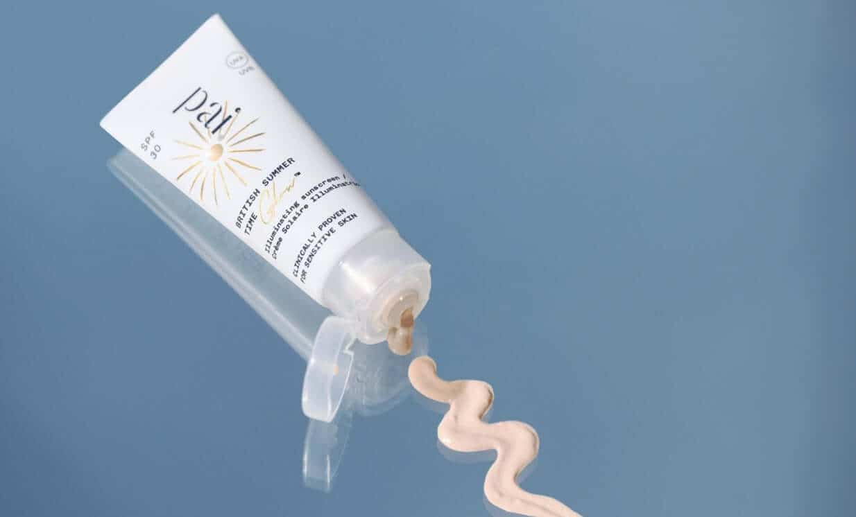 British Summer Time Glow SPF 30 sunscreen tube dispensing peach-tinted cream on blue background