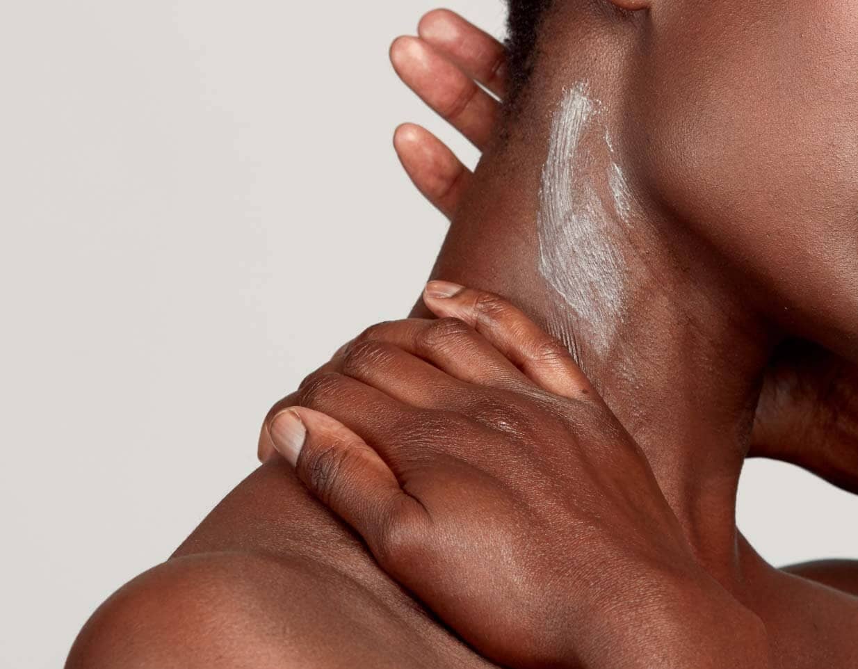 Hands applying white cream moisturiser to dark skin in gentle circular motions for body care routine