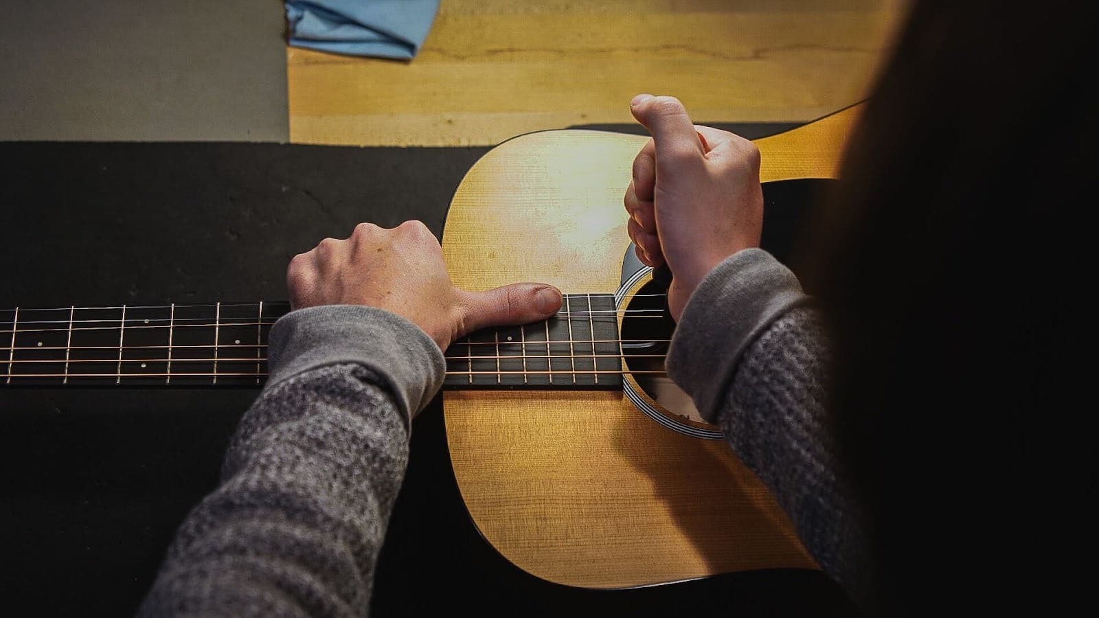Overhead view of a technician's hands checking the neck of a spruce-top guitar during an inspection