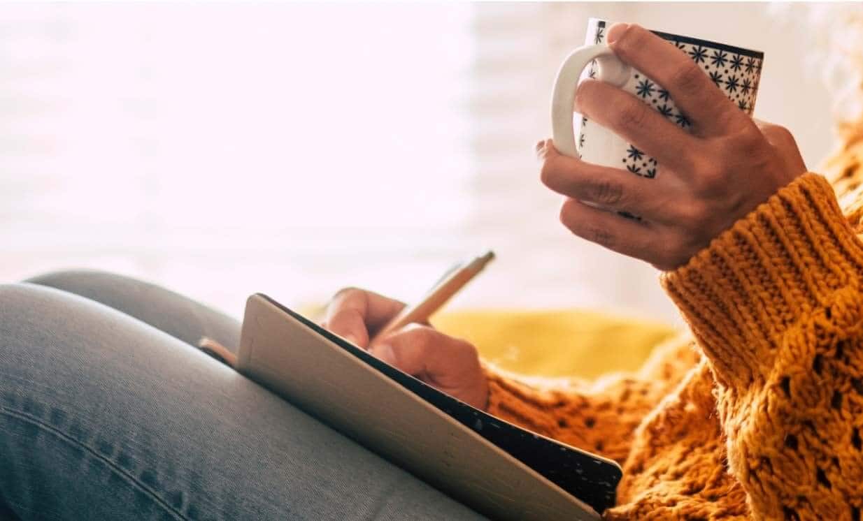 Person in orange sweater holding patterned mug while using tablet to track skincare routine and rosacea triggers