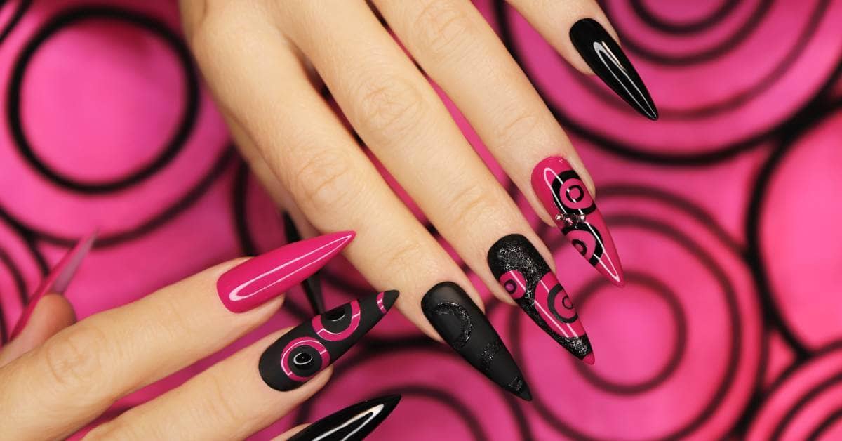 A close-up of pink and black long nail extensions. A few nails have a circular design on them while others don't.