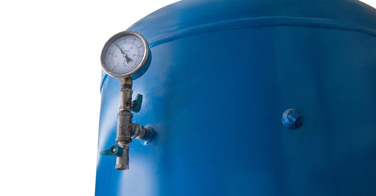Large blue compressed air receiver tank with a pressure gauge, valves, and metal fittings mounted on its side.